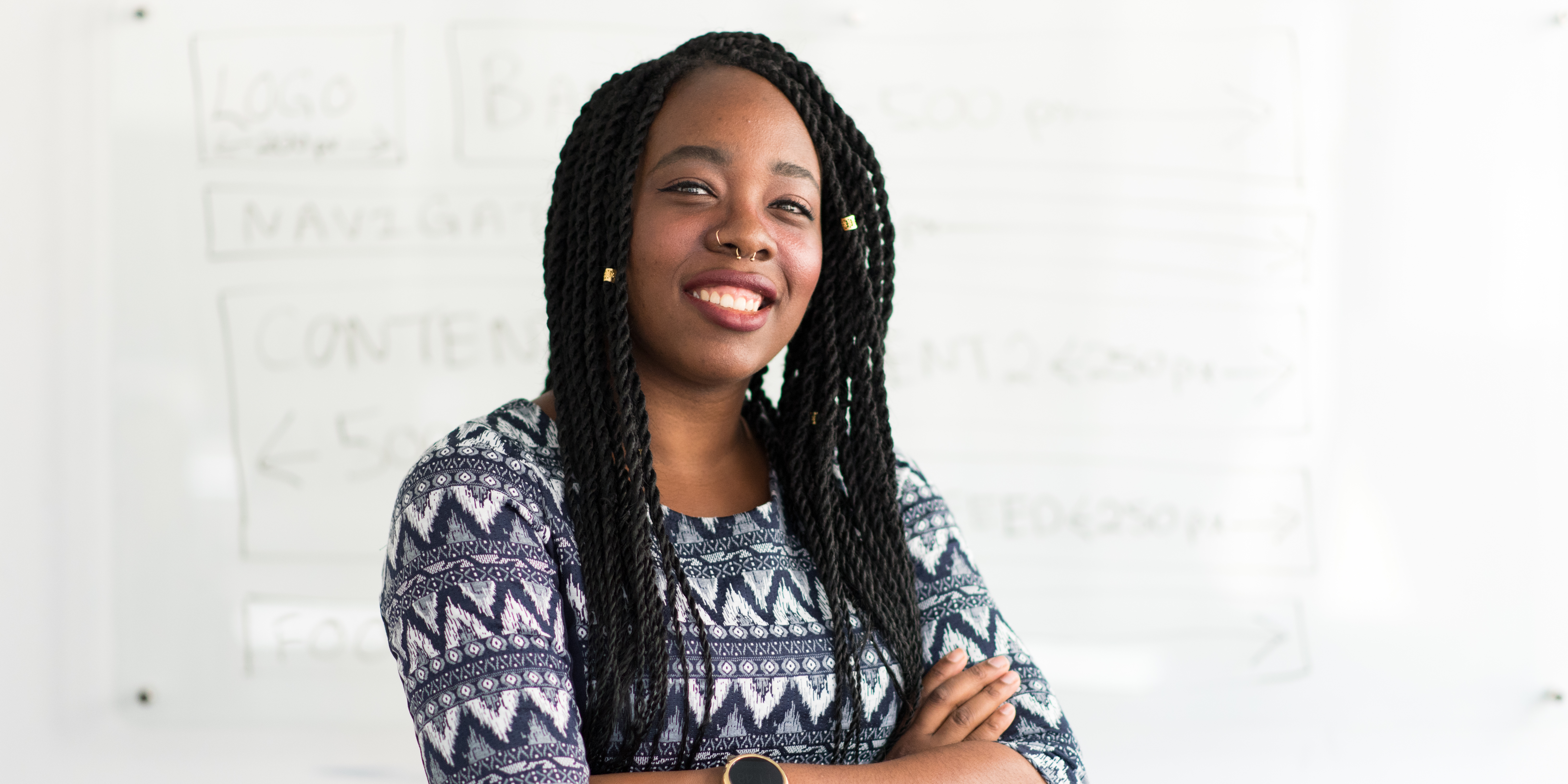 Person with long dark locs, septum ring, and arms crossed looks confidently at camera