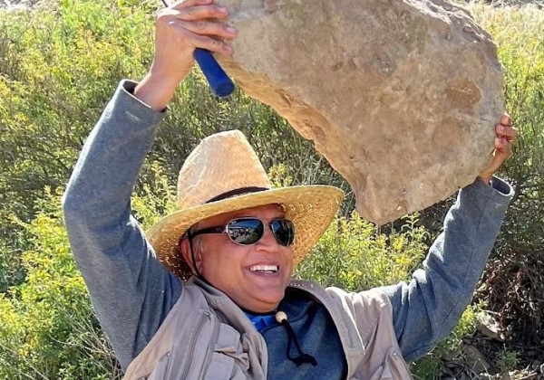 A man with sunglasses holding a rock smiling 
