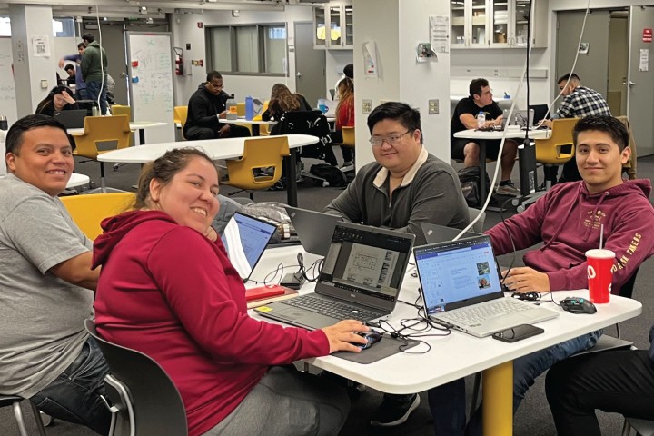 students gathered around table with laptops in CoLab smiling