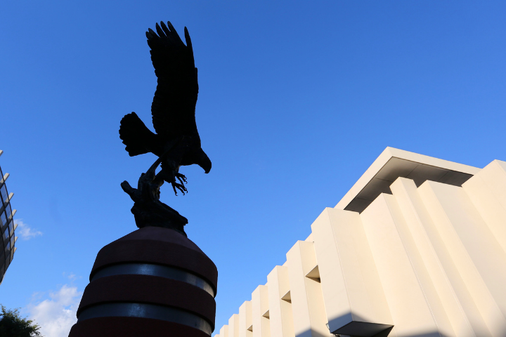 Eagle statue and white building behind. Backdrop is a blue sky 