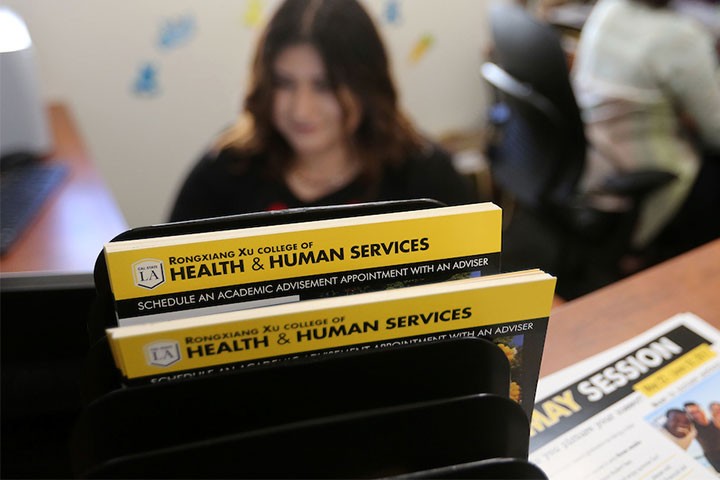 Rongxiang Xu College of Health and Human Services advising materials in front of staff member working at desk