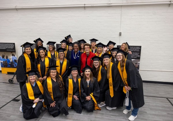 Graduates pose in caps and gowns with President Berenecea Johnson Eanes and Billie Jean King at a Cal State LA Prison Graduation Initiative event.