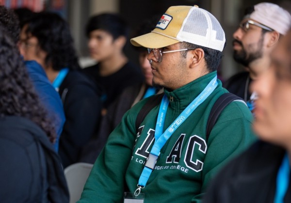 A student wearing a yellow cap and green sweatshirt with 'East Los Angeles College' lettering listens attentively during a STEM CORE session at Cal State LA.