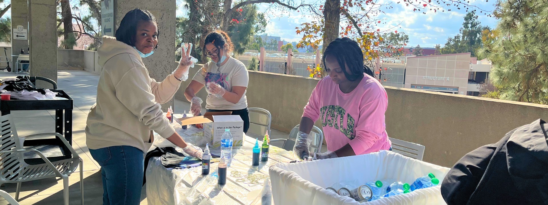 Three students smiling and creating a tie-dye shirt.