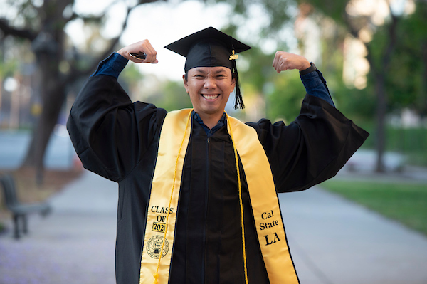 Cal State LA graduate with arms extended wearing black cap and gown.
