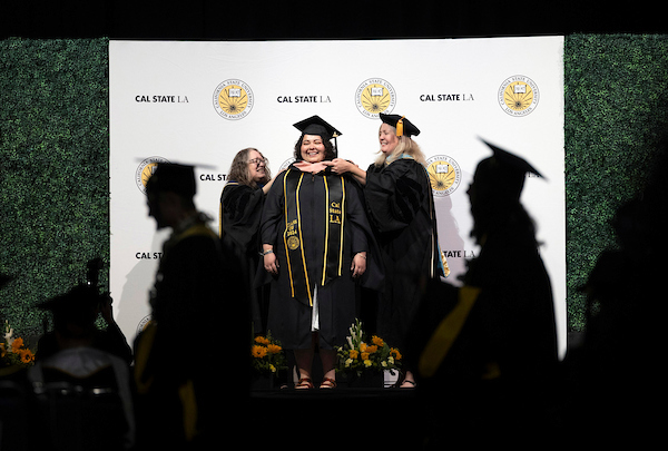 A student is hooded by two faculty members.