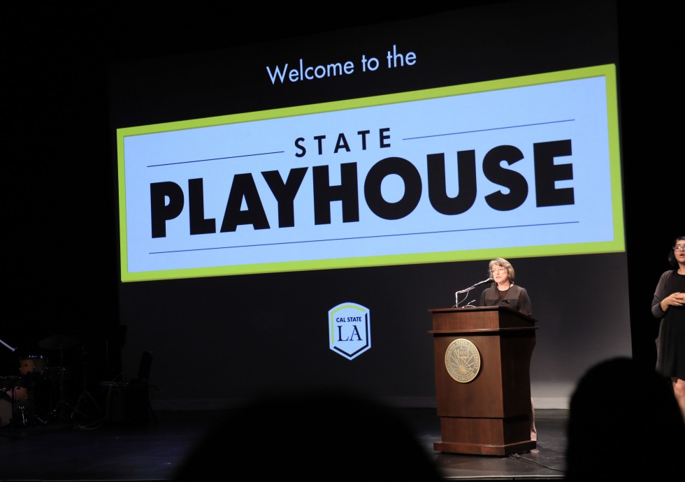 Dean Linda Essig at podium on stage of State Playhouse 