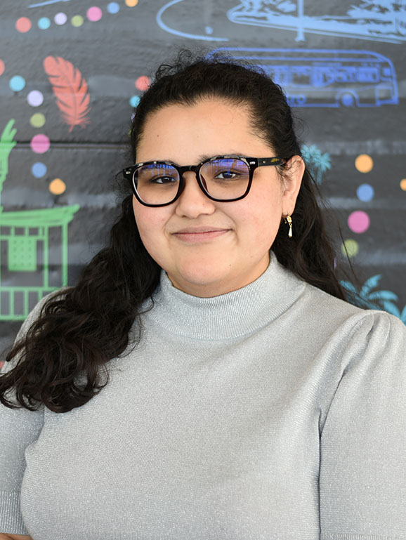 A person with long, curly hair wearing glasses and smiling.