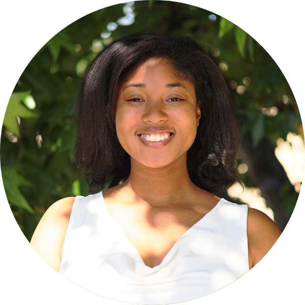 A woman with a white shirt smiling with leaves in the background.