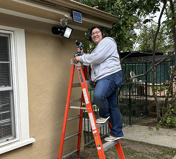 BOOST student Abby Installing solar security project on ladder
