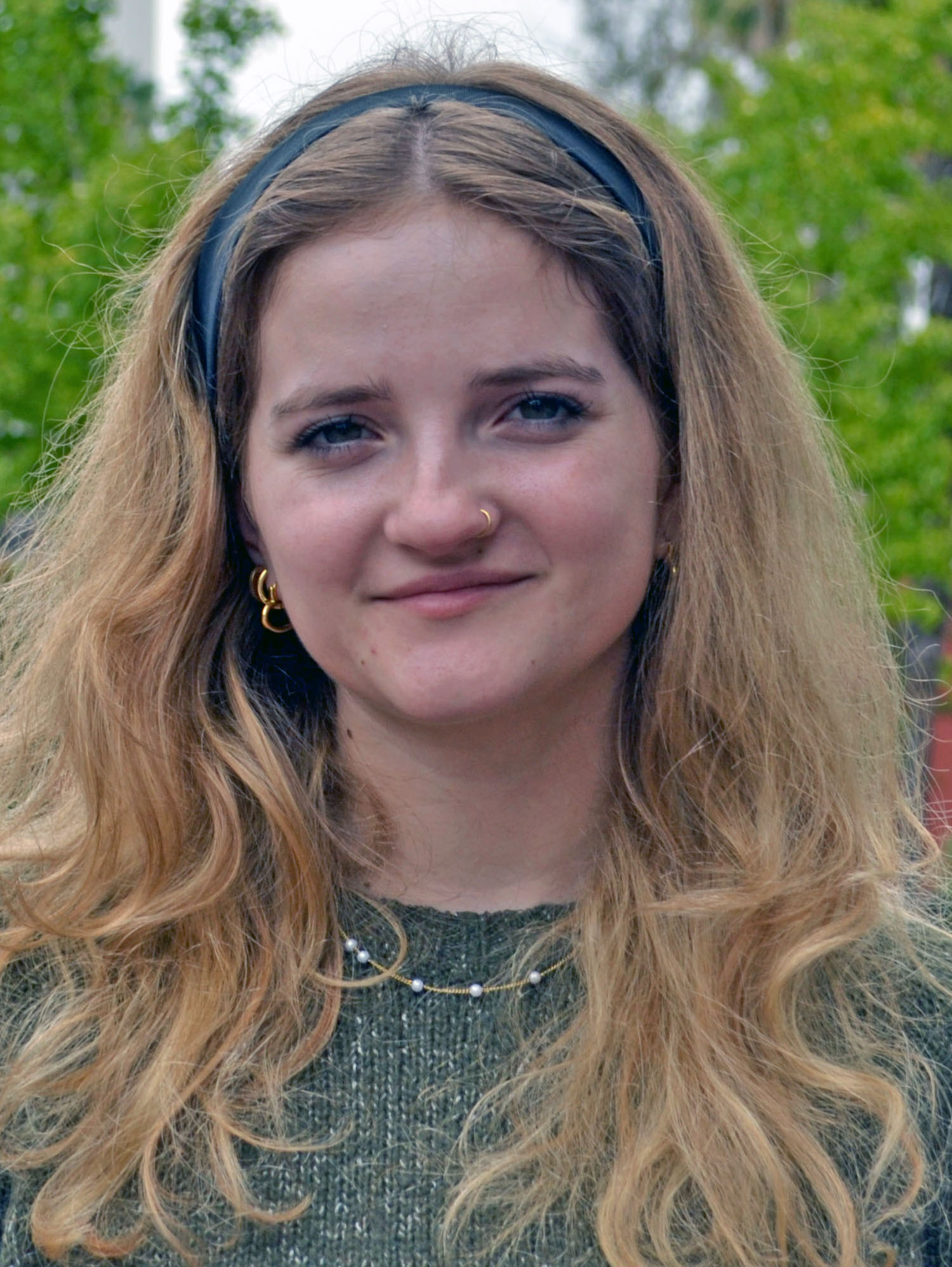 A person with long hair standing outside smiling.