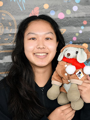 A person with long hair smiling, holding up a stuffed puppy.