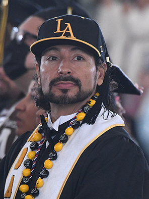 A person wearing graduation regalia and a Cal State LA baseball cap.
