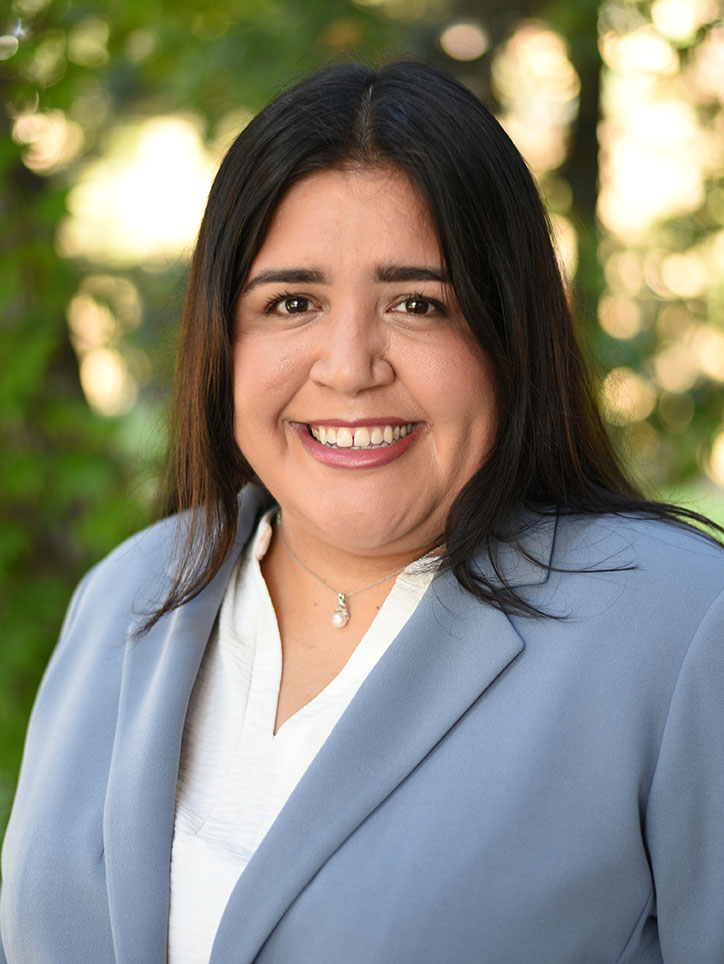 A person with long hair wearing a business jacket smiling.