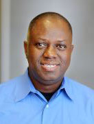 A person wearing a buttond-down shirt smiling.