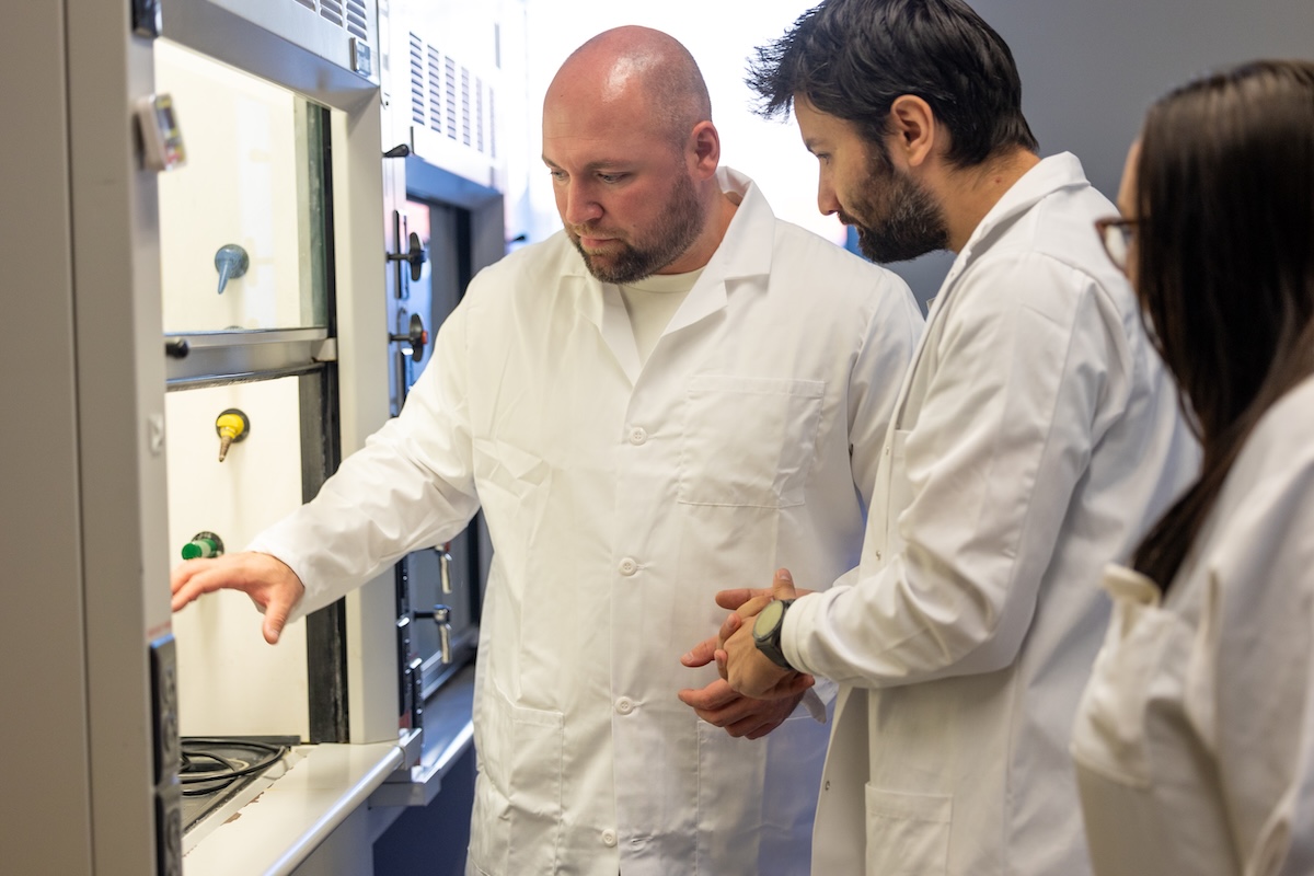 Petr Vozka and two researchers in white lab coats examine laboratory equipment.