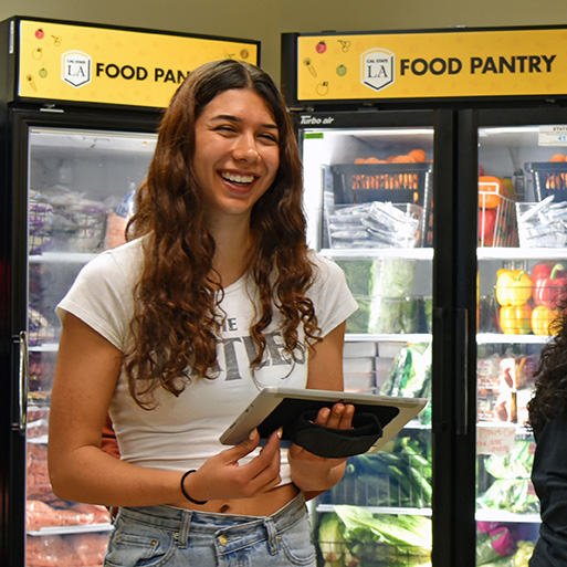 A student smiling and holding a clip board inside a food pantry.
