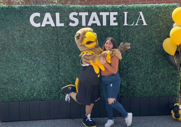 Eddie the Golden Eagle lifts leg while posing with a student.