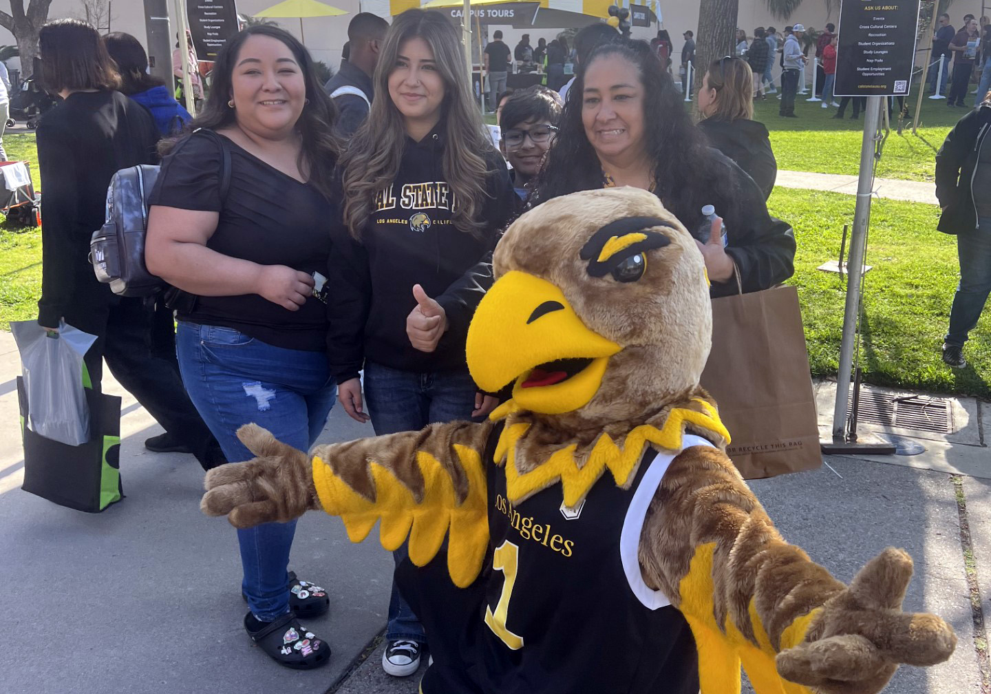 Eddie the Golden Eagle spreads arms open while posing with students.