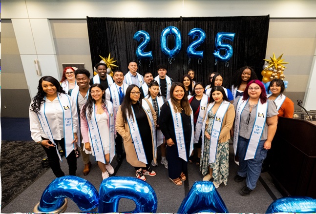 A group of people smiling wearing white and blue sashes.