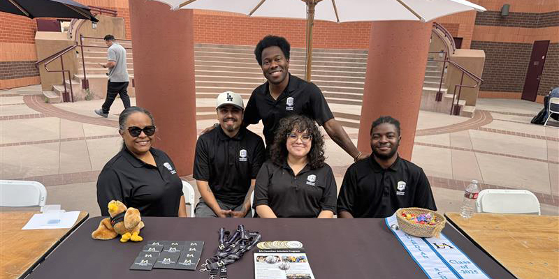Five people wearing matching polo shirts, sitting behind a table smiling.