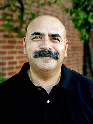 A person with a thick mustache smiling.