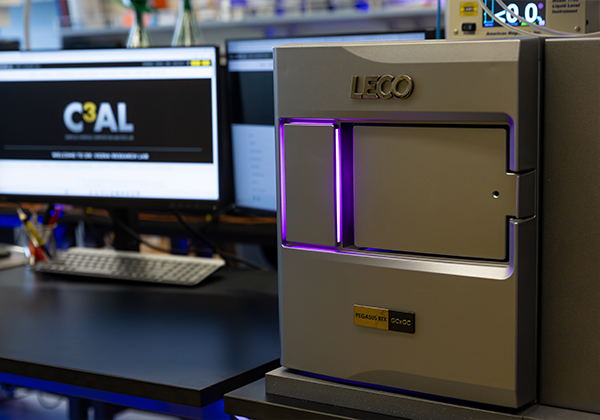 LECO Pegasus BTX mass spectrometer illuminated with a purple light in Cal State LA’s LECO Complex Chemical Compositional Analysis Lab, with computer monitors and lab equipment visible in the background.