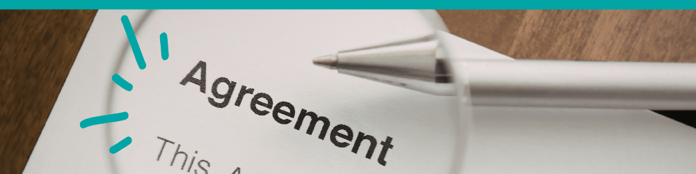 Agreement document under a magnifying glass with a pen.