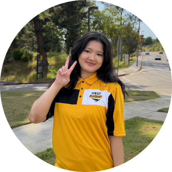 A woman with black hair and a yellow polo throwing a peace sign.