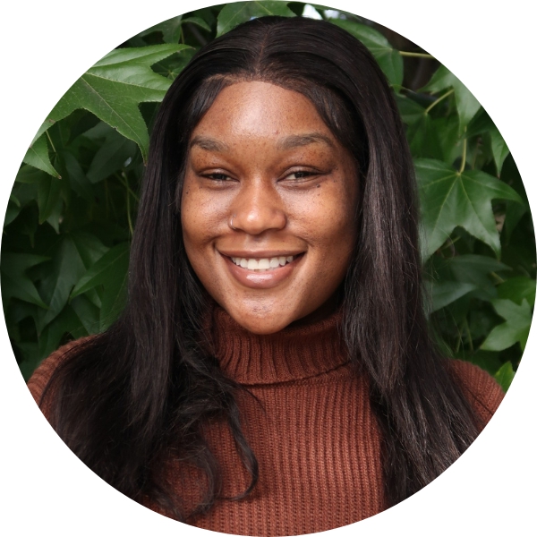 Woman with brown sweater smiling in front of leaves.