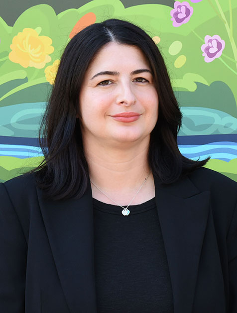 A person with dark, shoulder-length hair smiling slightly.