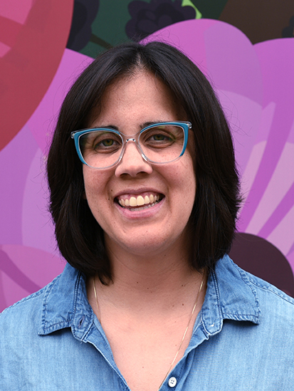 Person with shoulder-length hair and glasses smiling.