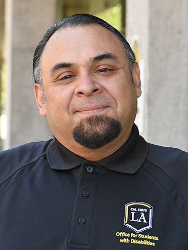 A person with facial hair smiling slightly.