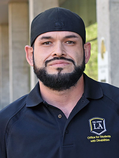 A person with a beard wearing a baseball cap backwards.