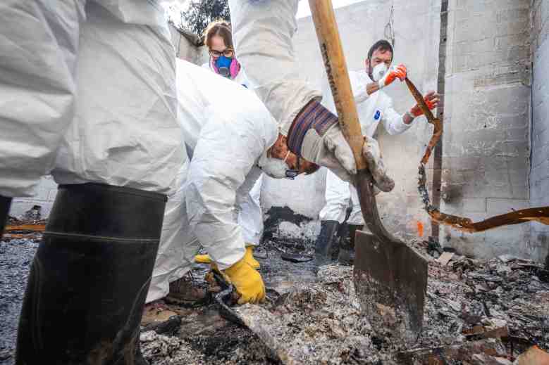 Close-up of archaeologists and volunteers digging through wildfire debris using shovels and gloved hands.