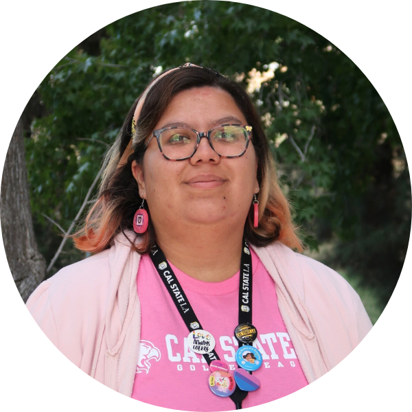 Woman in pink outfit and glasses smiling in front of foliage.