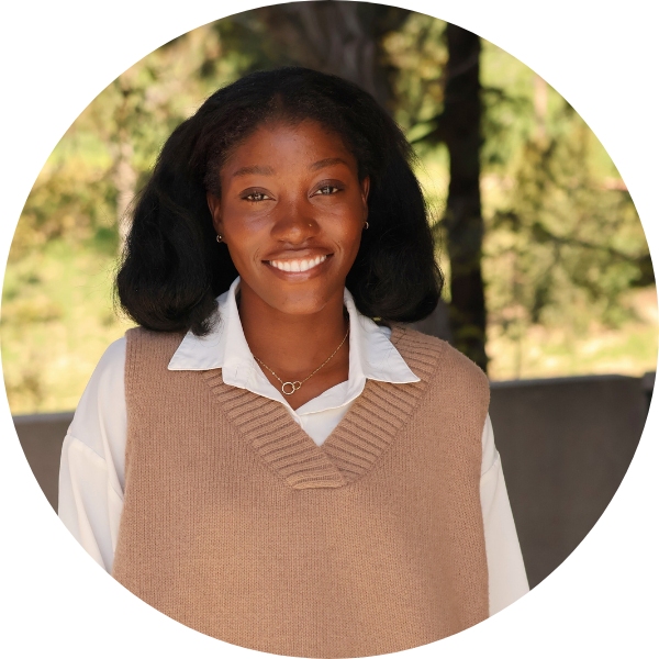 A woman with a white shirt and brown sweater vest smiling toward the camera.