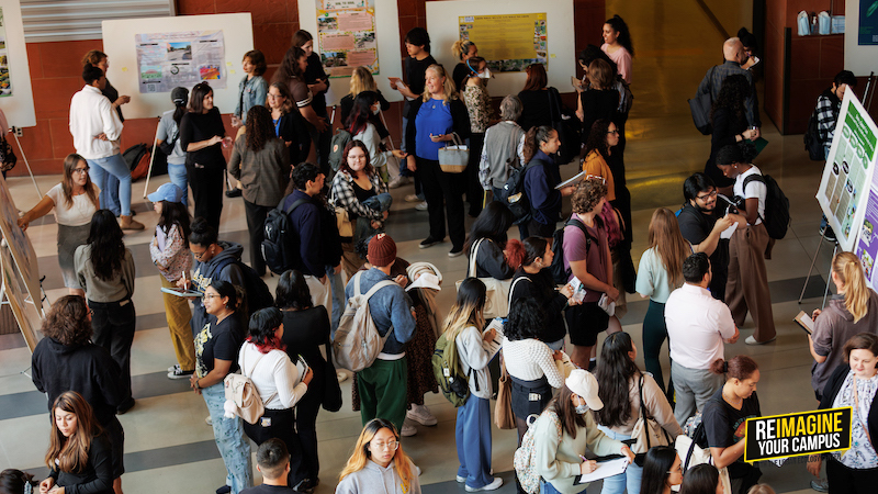 A busy event with people standing and reviewing poster presentations in an open indoor space