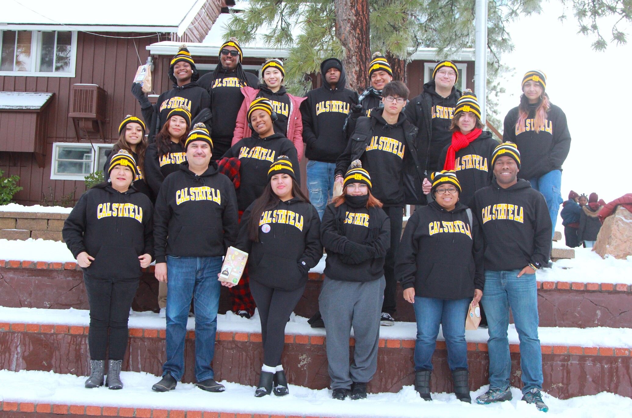 Group of students in black hoodies and sweaters smiling in snow.