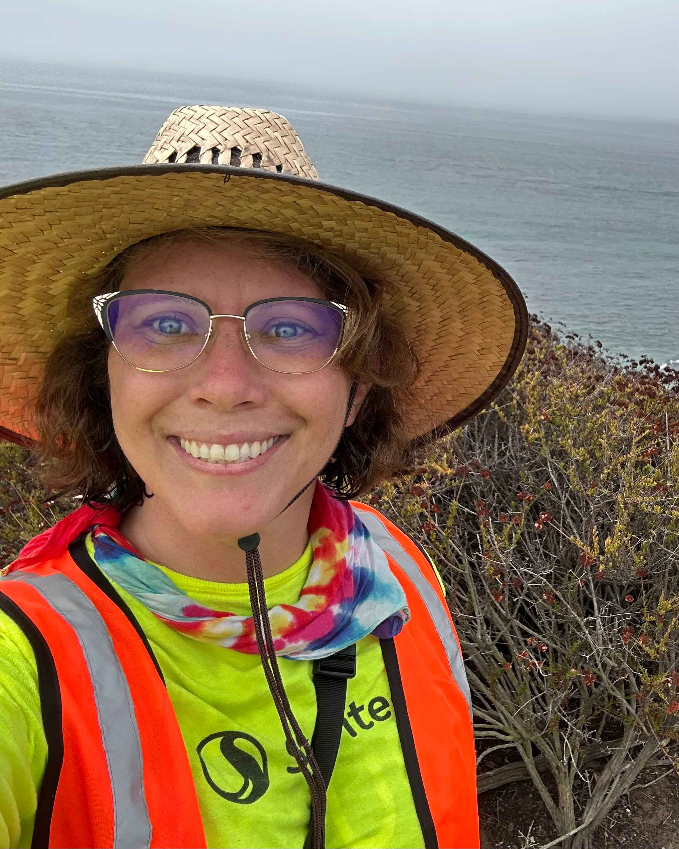 Grad Student wearing a wide brimmed hat smiling in the field at the coast.