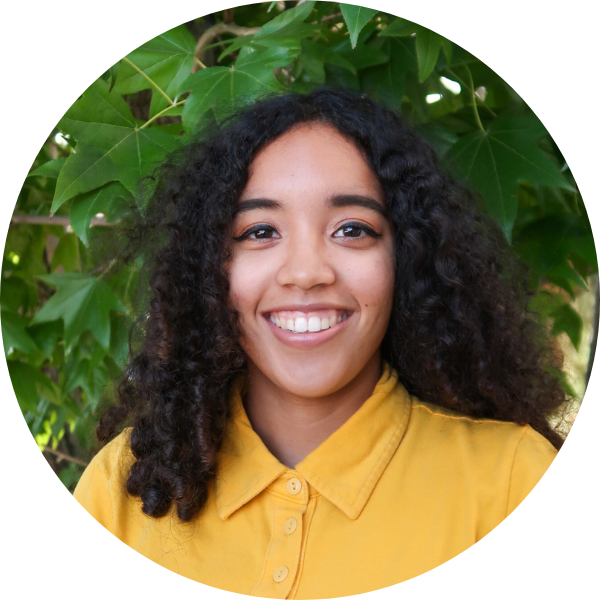 Woman with yellow shirt smiling in front of leaves.