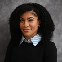 Photo of Young Woman in black sweater with blue collar shirt and black hair.