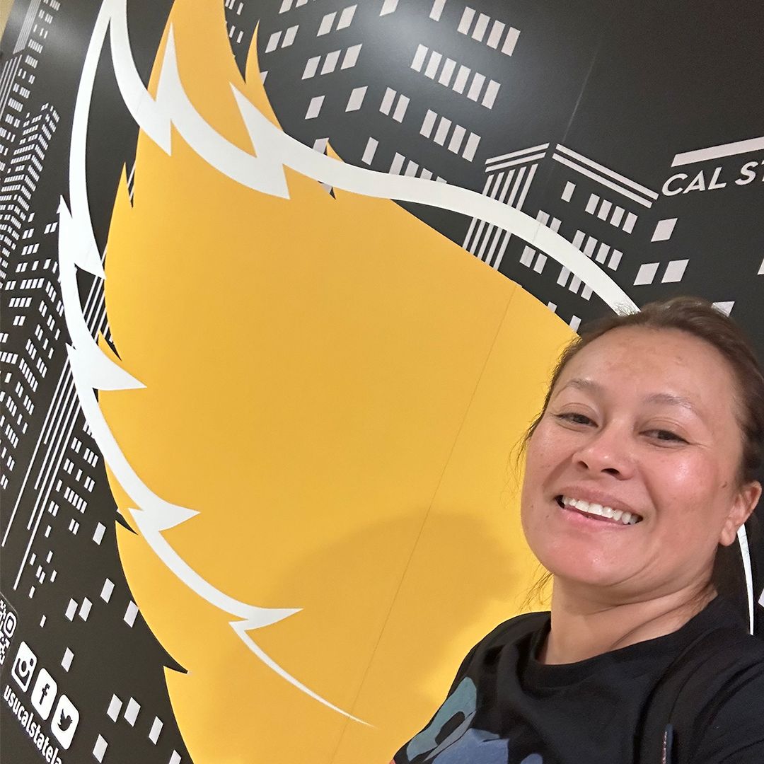 An individual in a black shirt taking a selfie against a yellow and black wall with a wing painted on it.