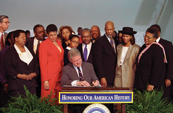 Roberts, third from the right, and other members of the Little Rock Nine watch as President Bill Clinton signs a bill making Little Rock Central High School a National Historic Site in 1998. Roberts received the Congressional Gold Medal in 1999. (Photo co