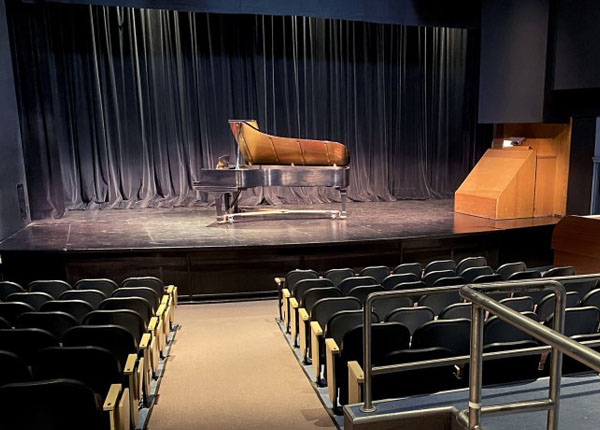 A music hall with a many seats and a large piano on the stage.