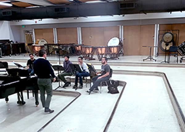 Students sitting by a piano inside of a music hall.