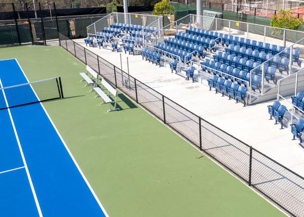 A tennis court and stadium style seats overseeing the tennis court.