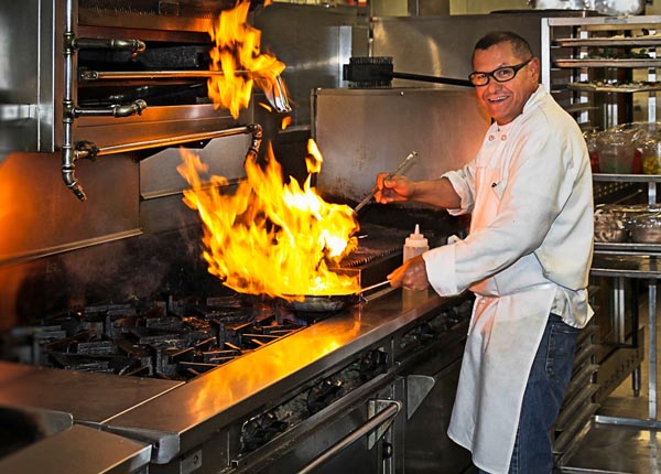 A chef using a frying pan over a stove.