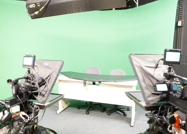 A news anchor table in front of a green screen.