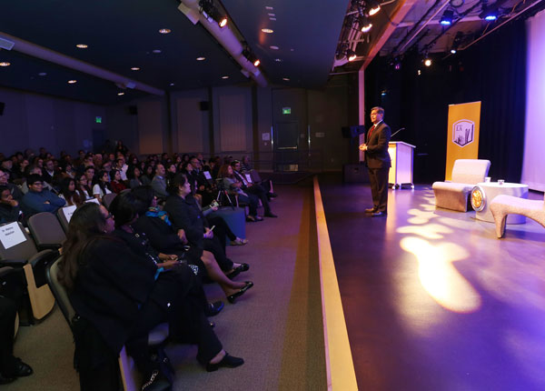 A person standing on a stage speaking to an audience.